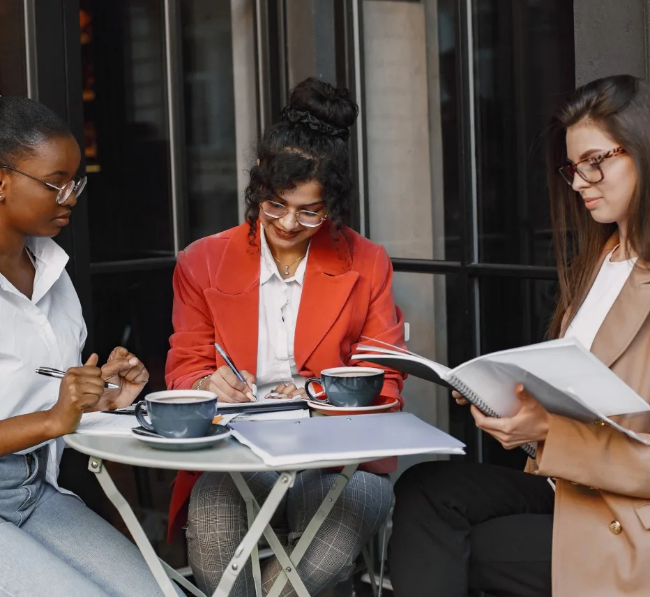 Women reviewing notes and papers together at a cafe table with coffee cups